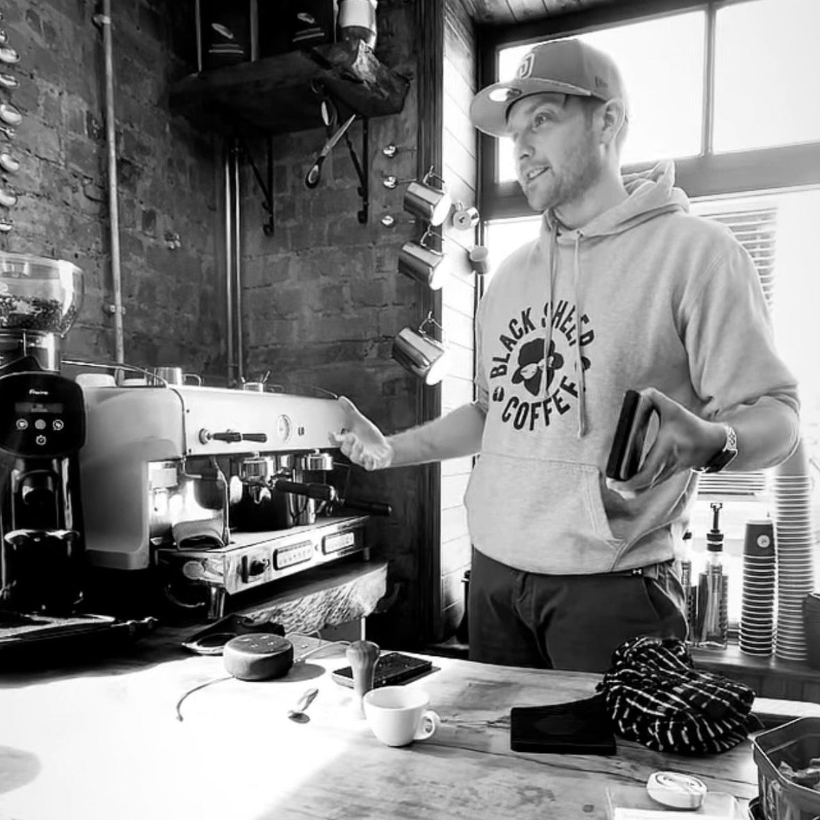 Person standing behind a counter with coffee equipment in a coffee shop.
